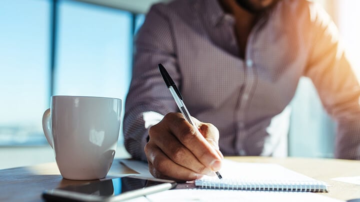 Man with coffee writing on paper