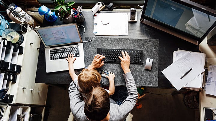 Uomo e bambino seduti alla scrivania mentre l'uomo scrive su un computer portatile e il bambino gioca con il cellulare