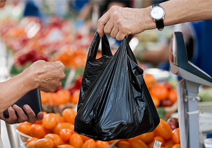 A black plastic bag is handed from one person to another in the fruit and vegetable section of a supermarket. 