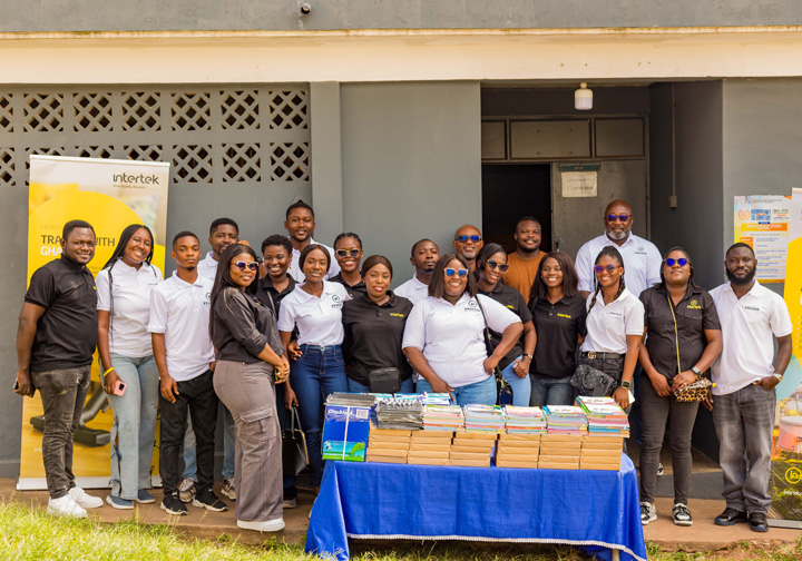 A team of 20 colleagues from Intertek Ghana stands behind a table of donated learning materials.