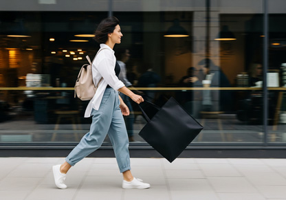 A woman walks along a road with a black tote bag in hand. 