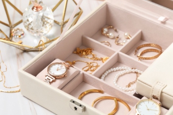 Jewelry box with many different accessories and perfume on white marble table, closeup