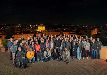A large group of Intertek colleagues poses for a picture on top of a building in Rome at night. 
