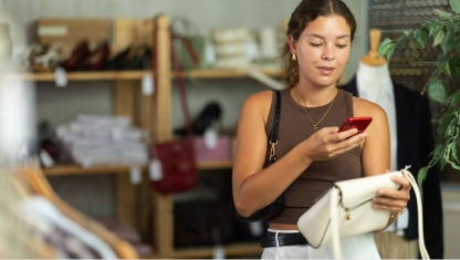 While shopping, girl scans barcode on label of handbag, verifies authenticity of eco-friendliness of clothing production. Responsible consumption..