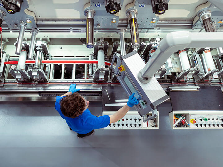 Aerial view of factory worker in blue shirt, safety glasses and gloves, at controls of an adhesive tape manufacturing machine