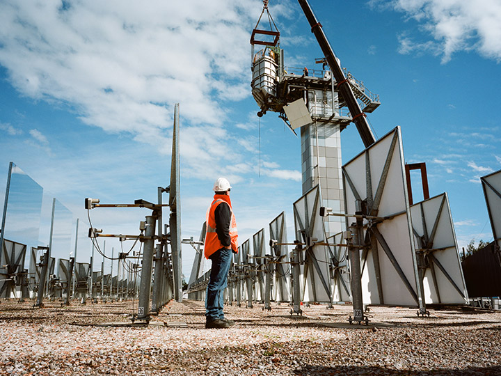 a worker stands in front of a mirror farm for thermal energy collection