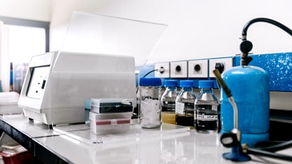 Laboratory setup with equipment, chemical bottles, and a blue gas cylinder on a clean workbench.