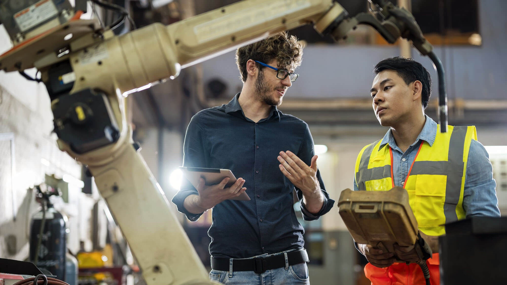 Software engineer explaining to controlling robotic welding process to welder in factory
